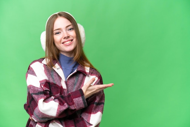 Jovem mulher bonita vestindo regalos de inverno sobre fundo croma isolado apresentando uma ideia enquanto olha para