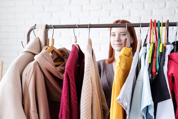 Jovem mulher bonita vestindo roupa da moda em pé perto de mudança de guarda-roupa de cabideiro