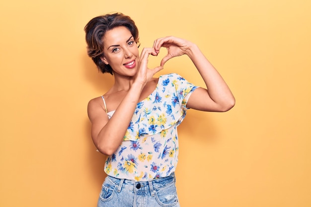 Jovem mulher bonita vestindo roupas casuais sorrindo apaixonadamente mostrando o símbolo do coração e a forma com as mãos conceito romântico