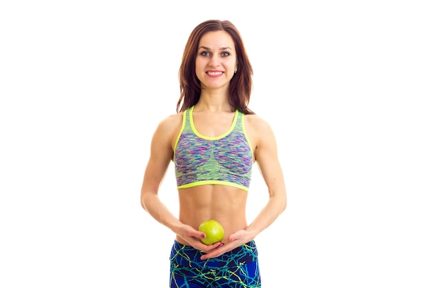 Jovem mulher bonita vestindo top de esportes coloridos comendo maçã verde em fundo branco no estúdio