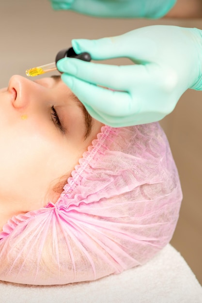 Jovem mulher branca recebendo retinol orgânico ácido pele do rosto com a pipeta em uma clínica de beleza