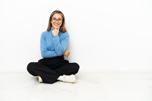 Jovem mulher branca sentada no chão com óculos e sorrindo