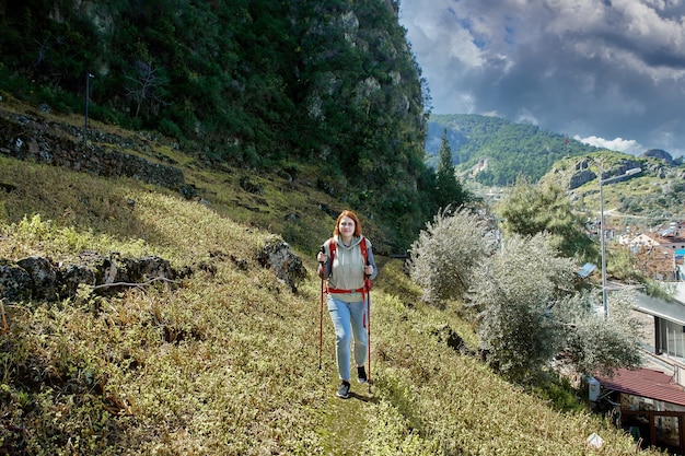 Jovem mulher branca usa vara de caminhada enquanto sobe uma encosta perto da cidade turística de Fethiye, na Turquia