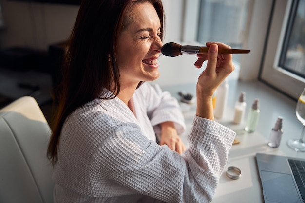 Jovem mulher brincalhona usando uma escova natural para se maquiar