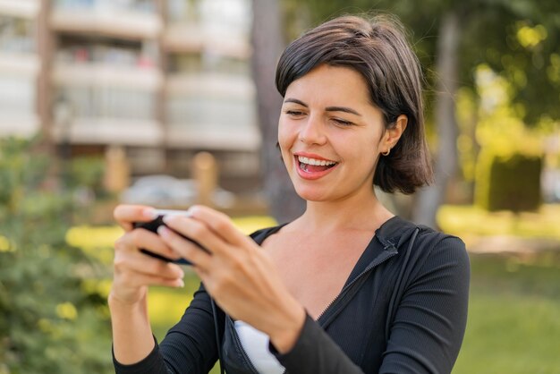 Jovem mulher búlgara bonita ao ar livre brincando com o celular