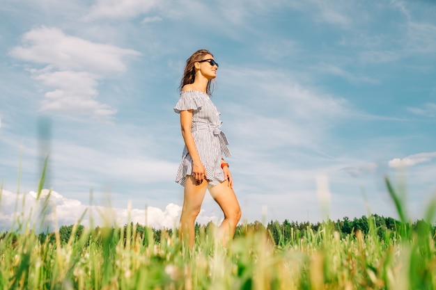 Jovem mulher caminhando no campo ensolarado verde