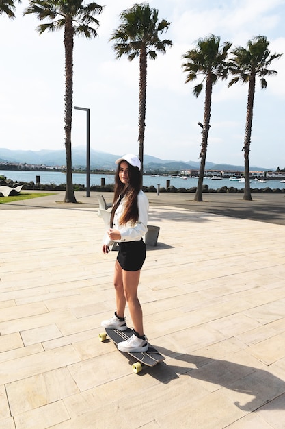 Jovem mulher caucasiana andando de longboard no calçadão