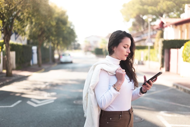 Jovem mulher caucasiana andando na rua usando um smartphone