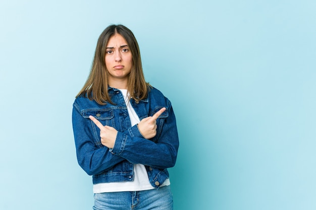 Jovem mulher caucasiana aponta para o lado, está tentando escolher entre duas opções.