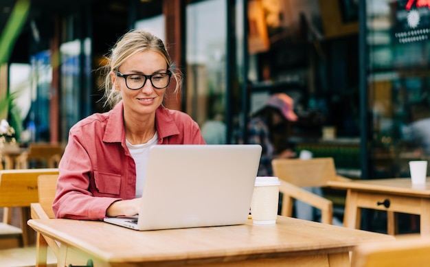 Jovem mulher caucasiana atraente sentada em um café trabalhando em um laptop