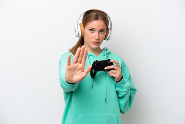 Jovem mulher caucasiana brincando com um controlador de videogame isolado no fundo branco, fazendo o gesto de parada
