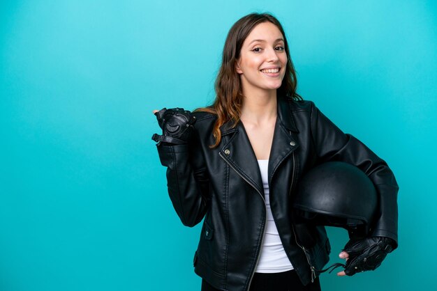 Jovem mulher caucasiana com capacete de moto isolado em fundo azul, apontando para o lado para apresentar um produto