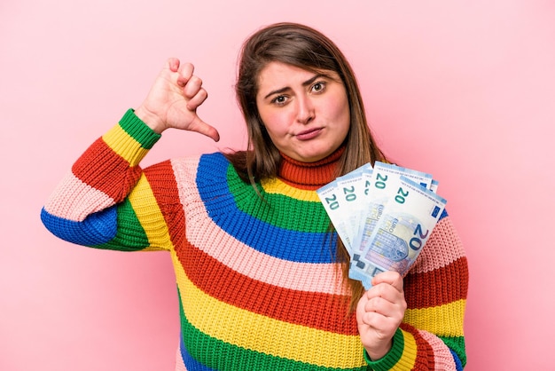 Jovem mulher caucasiana com excesso de peso segurando notas isoladas no fundo rosa sente-se orgulhosa e autoconfiante, exemplo a seguir.