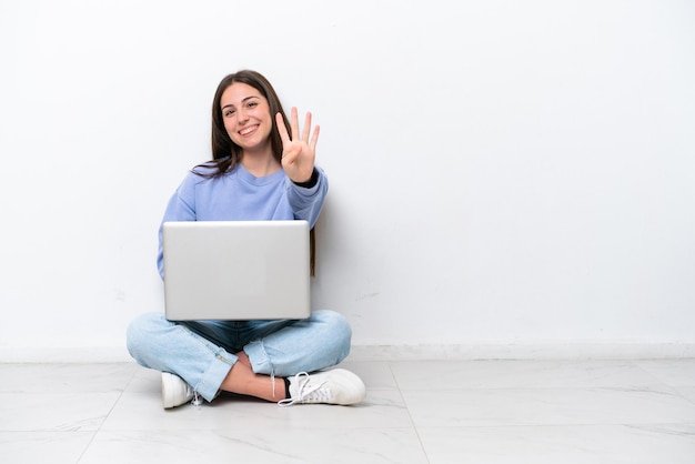 Jovem mulher caucasiana com laptop sentado no chão isolado no fundo branco feliz e contando quatro com os dedos