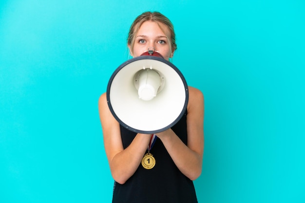 Foto jovem mulher caucasiana com medalhas isoladas em fundo azul gritando através de um megafone