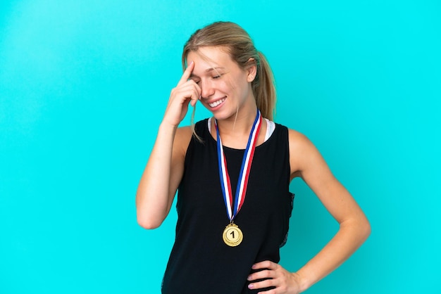 Jovem mulher caucasiana com medalhas isoladas em fundo azul rindo