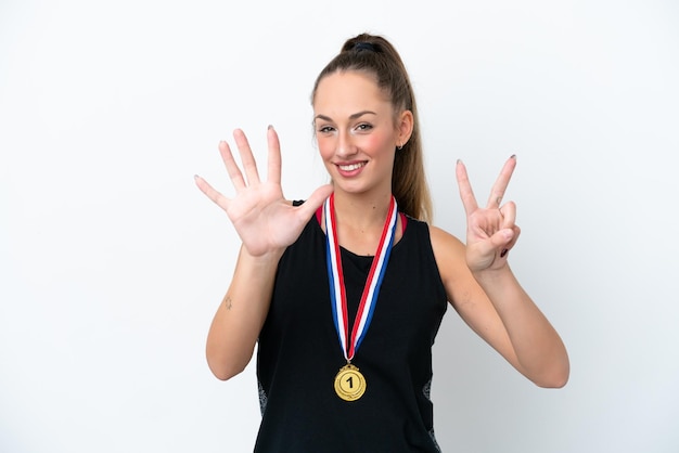 Foto jovem mulher caucasiana com medalhas isoladas em fundo branco contando sete com os dedos