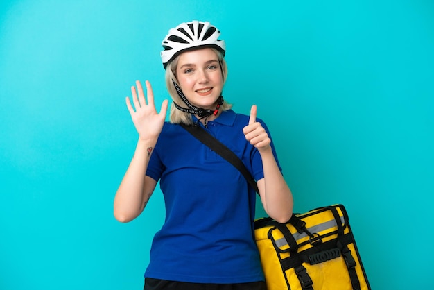 Jovem mulher caucasiana com mochila térmica isolada em fundo azul contando seis com os dedos