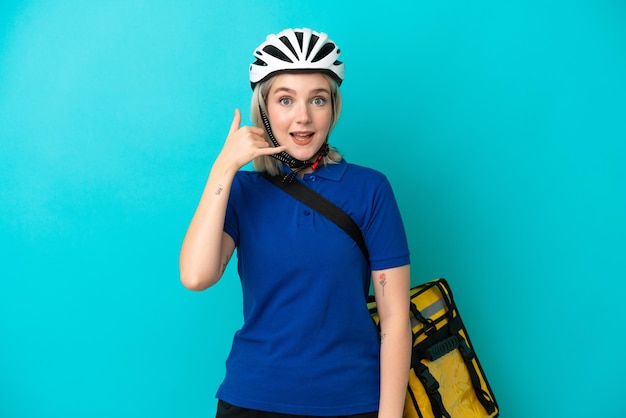 Jovem mulher caucasiana com mochila térmica isolada em fundo azul, fazendo gesto de telefone. Ligue-me de volta sinal