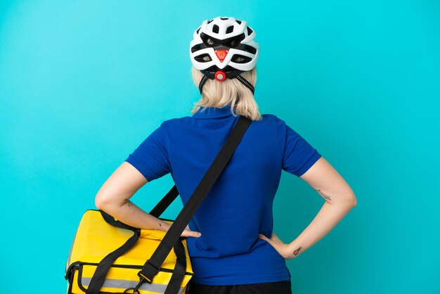 Foto jovem mulher caucasiana com mochila térmica isolada em fundo azul na posição traseira