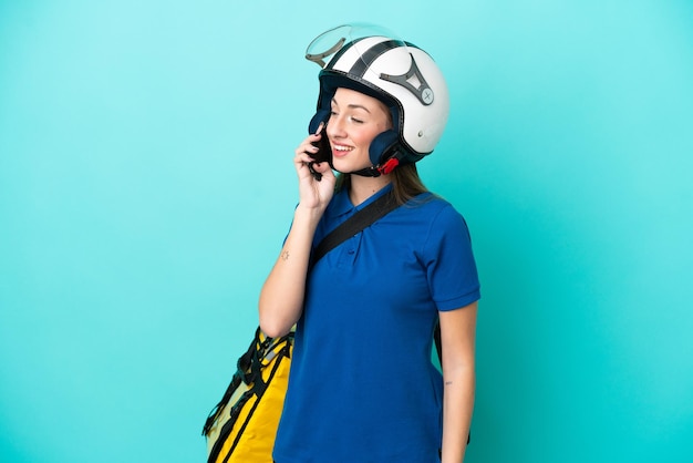 Jovem mulher caucasiana com mochila térmica isolada em fundo branco, mantendo uma conversa com o celular com alguém