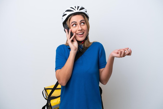 Jovem mulher caucasiana com mochila térmica isolada em fundo branco, mantendo uma conversa com o celular com alguém