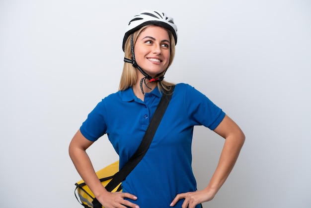 Jovem mulher caucasiana com mochila térmica isolada no fundo branco, posando com os braços na cintura e sorrindo