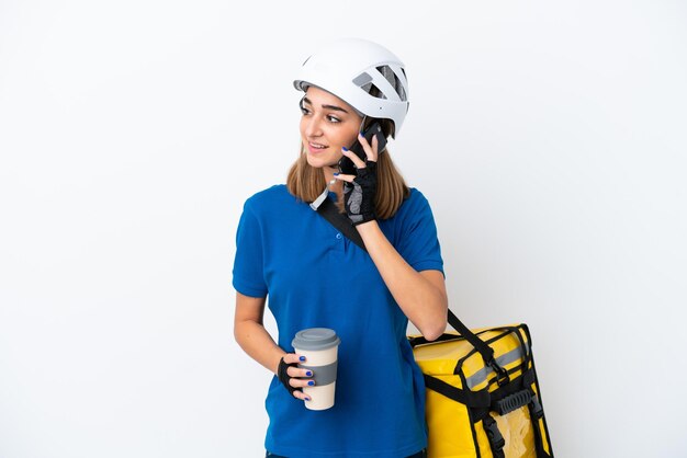 Jovem mulher caucasiana com mochila térmica isolada no fundo branco segurando um café para levar e um celular