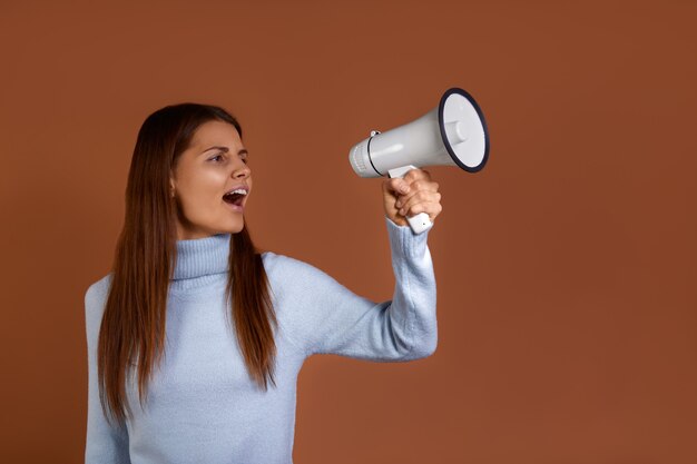 Jovem mulher caucasiana com suéter azul claro segurando um megafone na mão e gritando alto