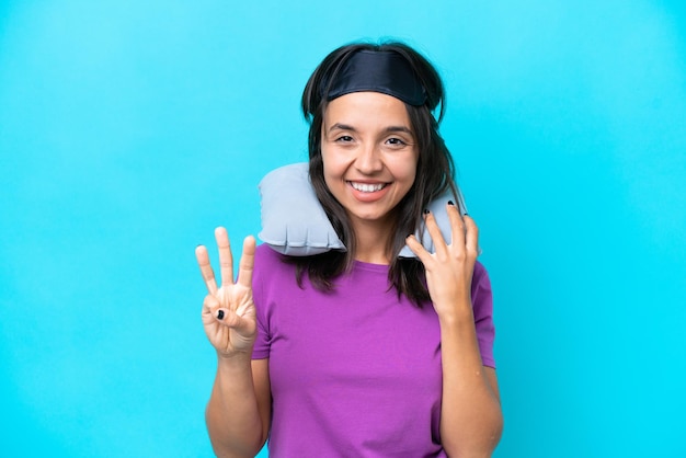 Jovem mulher caucasiana com travesseiro de viagem inflável isolado em fundo azul feliz e contando três com os dedos