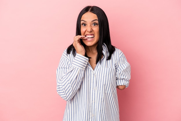 Jovem mulher caucasiana com um braço isolado no fundo rosa, roendo as unhas, nervosa e muito ansiosa.