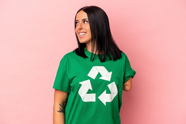 Jovem mulher caucasiana com um braço reciclado resíduos isolados no fundo rosa parece de lado sorrindo, alegre e agradável.