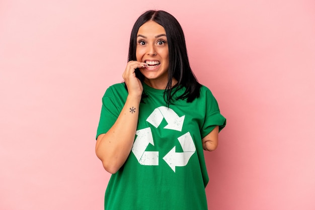 Jovem mulher caucasiana com um braço reciclado resíduos isolados no fundo rosa, roendo as unhas, nervosa e muito ansiosa.