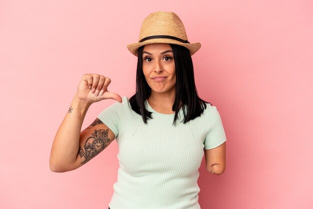 Jovem mulher caucasiana com um braço usando um chapéu de verão, isolado no fundo rosa, mostrando um gesto de antipatia, polegares para baixo. Conceito de desacordo.