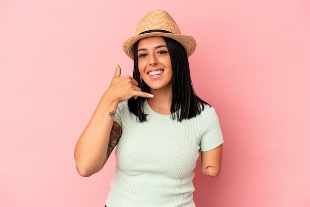 Jovem mulher caucasiana com um braço, usando um chapéu de verão, isolado no fundo rosa, mostrando um gesto de chamada de telefone móvel com os dedos.