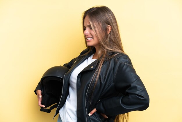 Foto jovem mulher caucasiana com um capacete de moto isolado em fundo amarelo, sofrendo de dor nas costas por ter feito um esforço