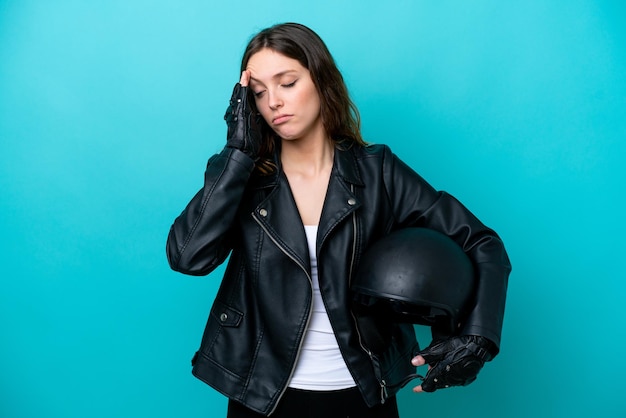 Jovem mulher caucasiana com um capacete de moto isolado em fundo azul com dor de cabeça