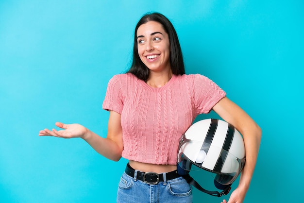 Jovem mulher caucasiana com um capacete de moto isolado em fundo azul com expressão de surpresa enquanto olha de lado