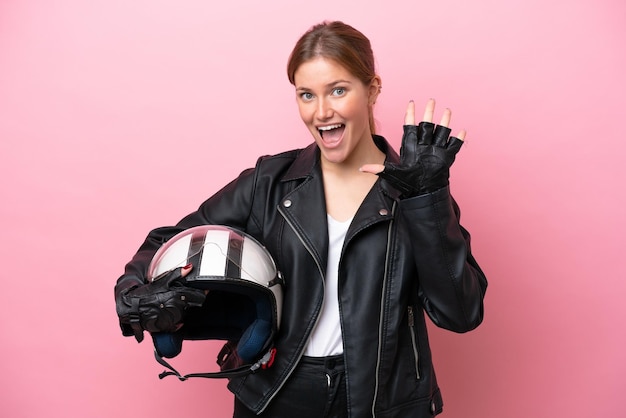 Jovem mulher caucasiana com um capacete de moto isolado em fundo rosa contando cinco com os dedos