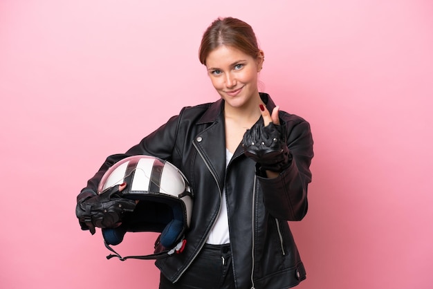 Jovem mulher caucasiana com um capacete de moto isolado em fundo rosa, fazendo gesto de dinheiro