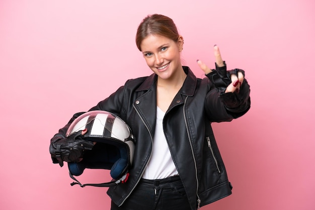 Jovem mulher caucasiana com um capacete de moto isolado em fundo rosa sorrindo e mostrando sinal de vitória