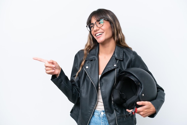 Jovem mulher caucasiana com um capacete de moto isolado no fundo branco, apontando o dedo para o lado e apresentando um produto