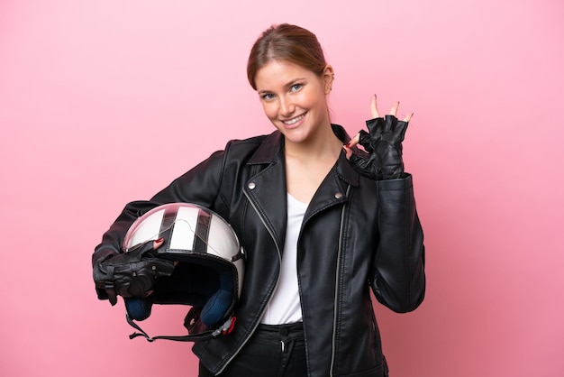 Jovem mulher caucasiana com um capacete de moto isolado no fundo rosa, mostrando sinal de ok com os dedos