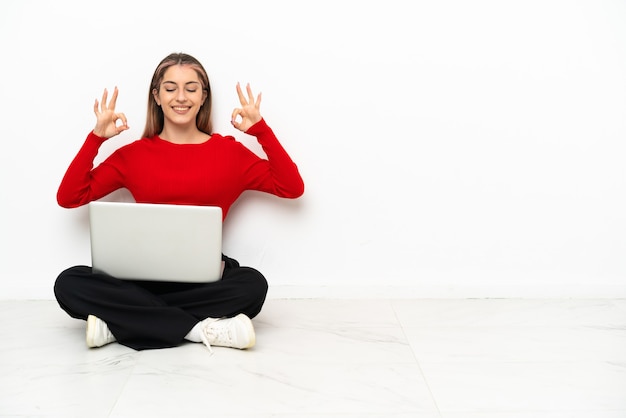 Jovem mulher caucasiana com um laptop sentada no chão em pose zen