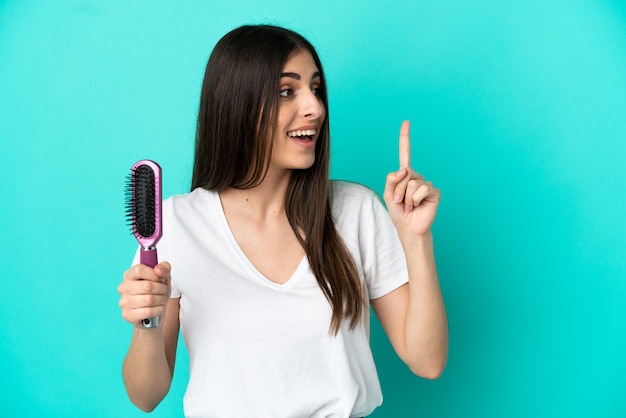 Jovem mulher caucasiana com um pente de cabelo isolado em um fundo azul com a intenção de perceber a solução enquanto levanta um dedo