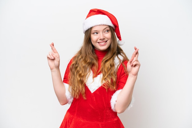 Jovem mulher caucasiana com vestido de Natal isolado no fundo branco com os dedos cruzados