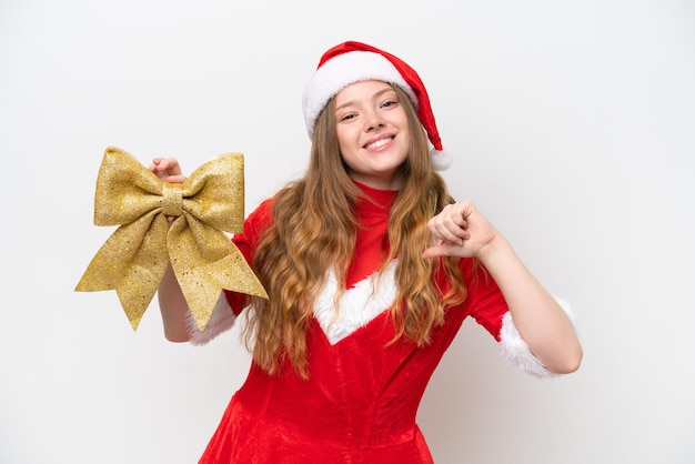 Jovem mulher caucasiana com vestido de Natal segurando laço de Natal isolado em fundo branco orgulhoso e satisfeito