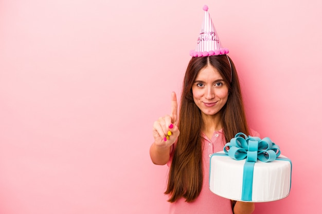 Jovem mulher caucasiana, comemorando um aniversário isolado no fundo rosa, mostrando o número um com o dedo.