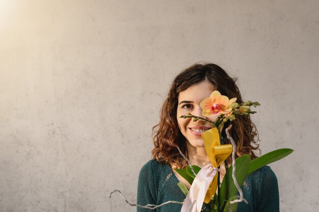 Jovem mulher caucasiana de retrato olhando para o sorriso de câmera com uma planta de orquídea amarela na frente do olho.