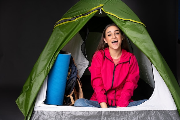 Foto jovem mulher caucasiana dentro de uma barraca de acampamento verde com expressão facial de surpresa